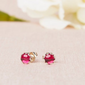 May include: A pair of silver stud earrings with a red gemstone in the center of each earring.