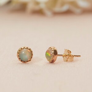 May include: A pair of gold stud earrings with iridescent opal stones. The earrings have a round shape with a scalloped gold setting. One earring is positioned to show the post and back.