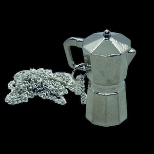 Puede incluir: Un collar de metal plateado con un colgante de metal plateado detallado y tridimensional en forma de cafetera.