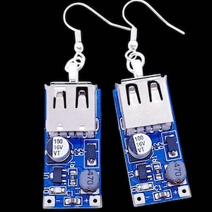 May include: A pair of unique earrings featuring a blue circuit board design with silver-tone USB ports and components. The earrings have silver-tone ear wires and are set against a black background.