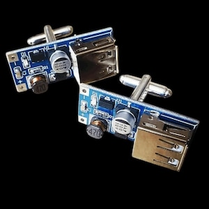 May include: A pair of cufflinks made from small circuit boards with USB ports and silver-toned metal clasps. The circuit boards are blue with black and white components.