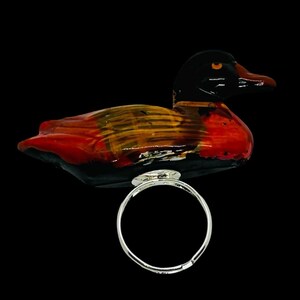 May include: A silver ring with a ceramic duck perched on top. The duck is painted in shades of red, orange, and black.