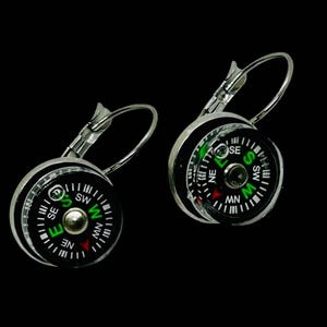 Puede incluir: Un par de pendientes de plata con forma de brújula con caras negras y agujas de brújula verdes. Los pendientes tienen un cierre de gancho de plata.
