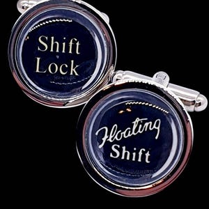 May include: A pair of silver cufflinks with a dark blue background. One cufflink reads "Shift Lock" in white script, and the other reads "Floating Shift". The cufflinks have a shiny, reflective finish.