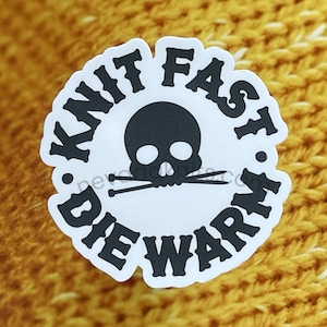 May include: A white circle sticker with black text that reads "Knit Fast Die Warm" and a black skull and crossbones in the center.