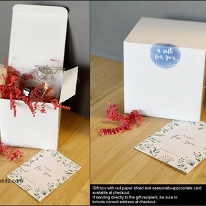 May include: A white gift box filled with red tissue paper and a clear glass ornament. The box has a sticker that says "a gift for you". A separate card with the same text is included.