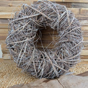 Könnte beinhalten: Ein natürlicher Rebenkranz mit kreisförmigem Design. Der Kranz besteht aus ineinander verschlungenen braunen Zweigen mit einem Hauch von silberner Farbe. Ein dekorativer Artikel für die Inneneinrichtung.