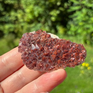 May include: A cluster of raw, crystalline mineral formation featuring deep reddish-brown and rust-colored points. The specimen displays a textured, jagged surface with numerous small, pointed crystal structures that catch the light, creating a sparkling appearance across the irregular, flattened shape of the stone.