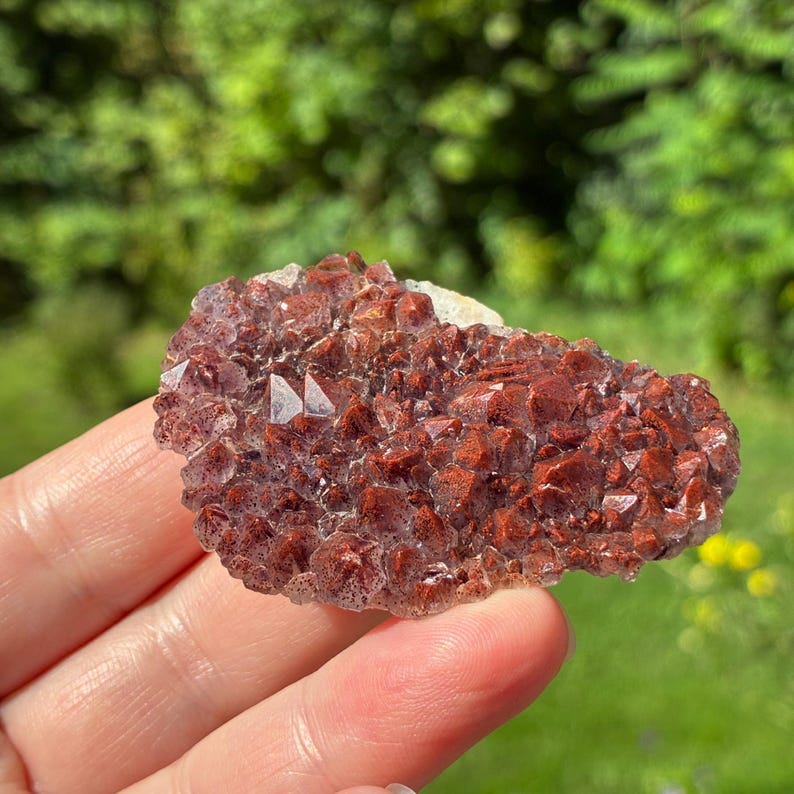 May include: A cluster of raw, crystalline mineral formation featuring deep reddish-brown and rust-colored points. The specimen displays a textured, jagged surface with numerous small, pointed crystal structures that catch the light, creating a sparkling appearance across the irregular, flattened shape of the stone.
