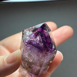 Op de afbeelding: Een doorschijnend, puntig kristalexemplaar met dieppaarse fantomen en insluitingen binnen zijn heldere, gefacetteerde structuur. Het mineraal vertoont scherpe geometrische randen en een duidelijk kleurverloop, overgaand van een donkerpaarse kern naar een lichtere, transparante basis met zichtbare interne breuken.