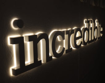 May include: A white sign with the word "incredible" in black letters with white outlines. The letters are illuminated from behind, creating a glowing effect.
