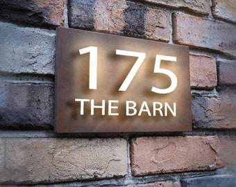May include: A brown metal house number sign with white lettering. The number 175 and the words "THE BARN" are displayed on the sign.