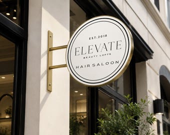 May include: A circular, double-sided metal sign with a gold-toned frame and mounting bracket. The white face features black circular borders and the text: EST. 2018, ELEVATE BEAUTY LOFTS, and HAIR SALOON, displayed in a clean, serif typeface.