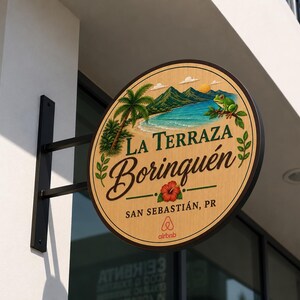 May include: A circular wooden sign mounted on a black metal bracket featuring a painted tropical landscape with a beach, mountains, a palm tree, and a green frog. The text reads La Terraza Borinqu&eacute;n, San Sebasti&aacute;n, PR, with an Airbnb logo below.
