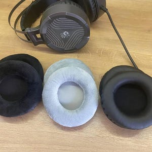 May include: Black and grey gaming headphones with three sets of replacement ear pads in black and light grey. The headphones have a mesh design on the earcups and a black cable.