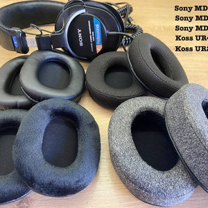May include: Assortment of black and gray ear pads for headphones. The ear pads are made of different materials, including leather, suede, and fabric. The ear pads are labeled with the following headphone models: Sony MDR 7506, Sony MDR-V6, Sony MDR-V7, Koss UR40, and Koss UR29.