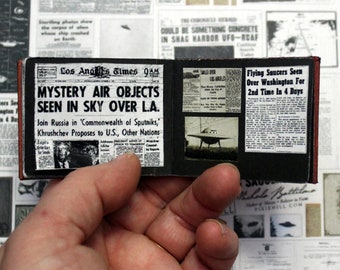 May include: A miniature scrapbook with newspaper clippings about flying saucers. The front page of the Los Angeles Times newspaper reads "Mystery Air Objects Seen in Sky Over L.A." and the other page reads "Flying Saucers Seen Over Washington For 2nd Time In 4 Days".