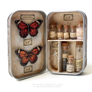 May include: A vintage tin box with a hinged lid, decorated with butterflies and musical notes. The box contains small glass vials with cork stoppers, filled with various items, including feathers, glitter, and dried flowers. The text on the box reads "Specimen", "No. 1 Chorus", "No. 2", "No. 3 Shrine", and "No. 4".