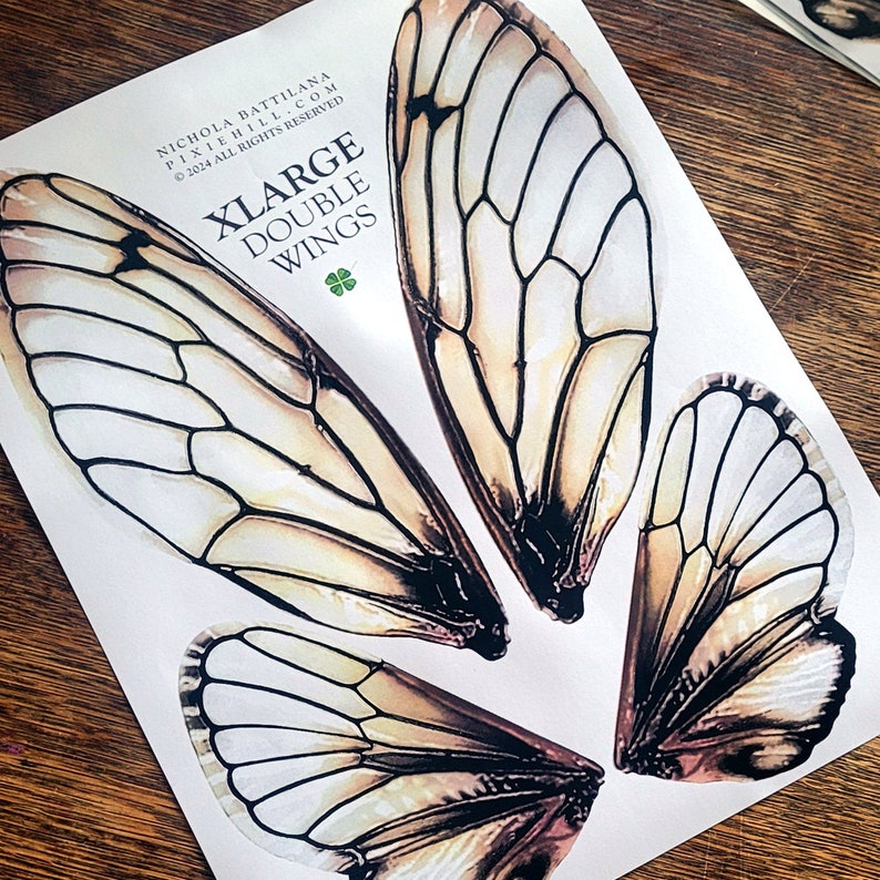 Puede incluir: Un conjunto de cuatro alas grandes dobles impresas en papel blanco. Las alas son de color marr&oacute;n claro con venas negras y un borde blanco. El texto "XLARGE DOUBLE WINGS" est&aacute; impreso en negro en la parte superior del papel.