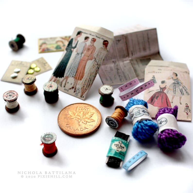 Op de afbeelding: Een verzameling miniatuur naaigerei, waaronder spoelen garen in verschillende kleuren, knopen, een Canadese cent en een vintage naaipatroon.