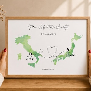 Peut inclure: Une impression encadrée présentant une carte aquarelle de l'Italie et du Japon en vert, reliées par une trajectoire de vol en pointillés formant un cœur. Le texte indique New Adventure Awaits, JULIA & AISHA, Italy, Japan et 3 MARCH 2026.