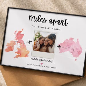 Pode incluir: Uma impressão emoldurada com o texto Miles apart BUT CLOSE AT HEART, um mapa em aguarela do Reino Unido e da Austrália com rotas de voo tracejadas, uma foto central estilo polaroid de três pessoas e os nomes Natalia, Monika & Aneta.