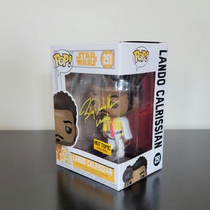 May include: A Funko Pop! vinyl figure of Lando Calrissian from Star Wars, in its original packaging. The box is white with the Star Wars and Pop! logos, and the figure is wearing a yellow shirt and white cape. The box reads "Lando Calrissian".