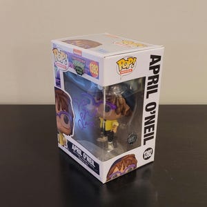 May include: A Funko Pop! Movies vinyl figure of April O'Neil from the Teenage Mutant Ninja Turtles franchise. The figure is wearing a yellow jacket, purple glasses, and a blue hat. The box is white with the Funko Pop! logo and the Teenage Mutant Ninja Turtles logo. The figure is numbered 1392.