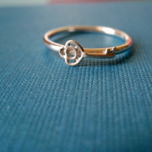 May include: A silver key ring with a decorative key charm. The key charm is shaped like a flower with a small hole in the center. The ring is on a blue surface.