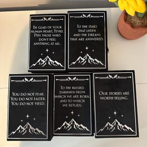 May include: Five black velvet-covered boxes with silver lettering and mountain imagery. The boxes have quotes about darkness, stars, and stories.