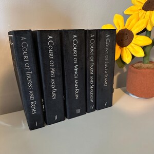 May include: A set of five black hardback books with silver lettering. The titles are "A Court of Thorns and Roses", "A Court of Mist and Fury", "A Court of Wings and Ruin", "A Court of Frost and Starlight", and "A Court of Silver Flames".