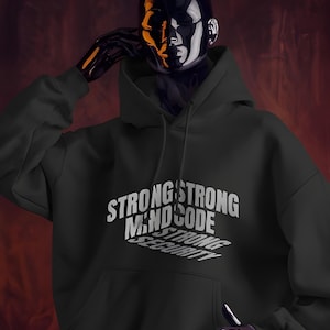 Op de afbeelding: Zwarte hoodie met de witte tekst "STRONG MIND CODE SECURITY", gestapeld en schuin over de voorkant. De hoodie heeft een capuchon en een voorzak. De achtergrond is donkerrood.