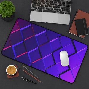 Peut inclure: Tapis de souris rectangulaire avec un motif géométrique de cubes violets et bleus. Une souris d'ordinateur blanche est posée sur le tapis. Un ordinateur portable, des cahiers, une tasse de café et des crayons sont également sur le bureau.