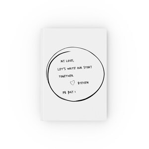 May include: A white notebook with a black circle and the text "My love, let's write our story together. P.S. Day 1" inside the circle. The text "Steven" is written next to a small heart symbol.