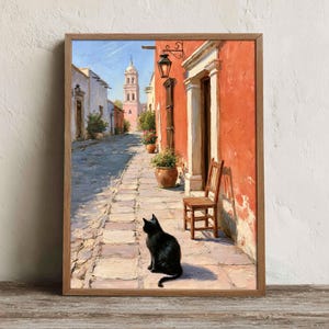 May include: A framed oil painting depicting a sunlit cobblestone street in a Mediterranean town. A black cat sits in the foreground, facing a wooden chair, potted plants, and a tall bell tower under a clear blue sky against a vibrant orange wall.