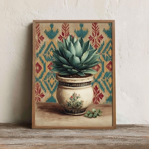 May include: A framed wall art print featuring a green succulent plant in a cream-coloured ceramic pot with a floral motif. The background displays a repeating geometric pattern in shades of teal, yellow, and red, set within a light wood frame.