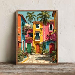 Puede incluir: Una impresión enmarcada de una colorida escena callejera. Edificios en tonos naranja, azul, rosa y amarillo bordean una calle adoquinada. Las palmeras y las plantas con flores se suman al ambiente tropical. La obra de arte está enmarcada en un marco de madera clara.