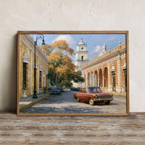 May include: A framed painting depicting a street scene with a vintage red sedan parked on a cobblestone road. The scene features yellow colonial-style buildings with arched walkways, a tall clock tower, and a large tree with golden autumn leaves.