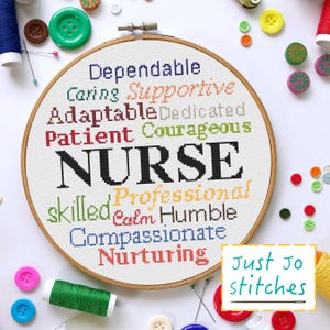 May include: A white embroidery hoop with the word "NURSE" in large black letters surrounded by a circle of words describing the qualities of a nurse, including "dependable", "caring", "supportive", "adaptable", "dedicated", "patient", "courageous", "skilled", "professional", "calm", "humble", "compassionate", and "nurturing". The words are in different colors. The hoop is on a white surface with colorful buttons and embroidery floss scattered around it. The text "Just Jo stitches" is in the lower right corner of the image.