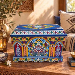 May include: A rectangular wooden chest featuring a vibrant blue base colour with intricate, multi-coloured floral and geometric patterns in red, yellow, green, and white. The design includes arched motifs and detailed scrollwork across the lid and sides.