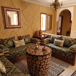 Peut inclure: Un salon avec une table basse cylindrique faite de tranches de bois, des canapés en L au revêtement vert foncé à motifs, un miroir à cadre en cuivre, un lustre en métal et un tapis géométrique noir et blanc au sol.