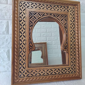 Peut inclure: Un miroir en bois avec un cadre sculpté complexe. Le cadre présente un motif géométrique en noir et brun. Le miroir a une ouverture en arc.
