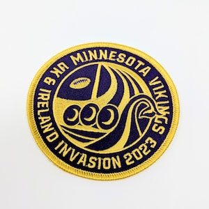 May include: A gold and purple embroidered patch with the text "Minnesota Vikings Ireland Invasion 2023" and a stylized image of a ship with three footballs.