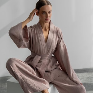 Peut inclure: Un ensemble de détente deux pièces couleur vieux rose composé d'un haut style kimono à manches longues avec une ceinture à nouer assortie et d'un pantalon large. Le tissu présente une texture froissée sur tout le vêtement.