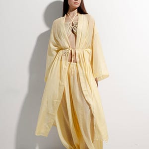 May include: A pale yellow three-piece ensemble: a halter top, harem trousers, and a long, open-front robe. The robe features wide sleeves and a tie at the waist. The trousers have gathered ankles. The outfit is crafted from a lightweight, flowing material.
