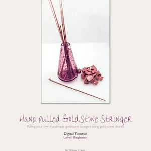 Puede incluir: Una botella de vidrio púrpura con un cordón de piedra dorada en su interior. La botella está sobre una superficie blanca con un montón de trozos de piedra dorada al lado. La botella tiene una superficie texturizada y un cuello estrecho. El cordón de piedra dorada está hecho de finas hebras doradas. Los trozos de piedra dorada son de forma irregular y tienen un brillo metálico.