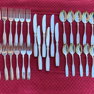May include: A collection of stainless steel flatware consisting of twelve forks, six knives, and twelve spoons arranged in rows. The set features a simple, polished design with slender handles and smooth, rounded edges on the spoon bowls and fork tines.