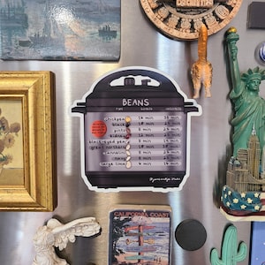 May include: A white magnet with a black and white illustration of a pressure cooker with a chart listing different types of beans and their cooking times in a pressure cooker. The chart includes the following beans: chickpea, black, pinto, kidney, black-eyed pea, great northern, cannellini, navy, and large lima. The chart lists the cooking times for both soaked and unsoaked beans.
