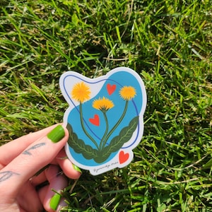 May include: A sticker with a blue background and three yellow dandelions with red hearts. The sticker has the text "Pjarencage Studio" at the bottom.