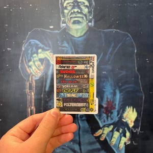 May include: A white sticker with a collage of horror movie VHS tapes. The titles include "Friday the 13th", "Nightmare", "Halloween", "The Evil Dead", "Scream", "The Fly", "Thing", "The Exorcist", "Poltergeist", and "Alien".